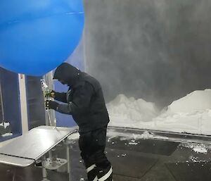 A person in full protective gear works with a blue balloon
