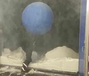 A person in black walks through a door into snow holding a blue balloon