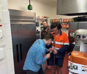 Two men working on pipe in kitchen with a third looking over their shoulders at their work
