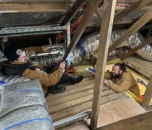 Two men in the roof of a building, working on duct work