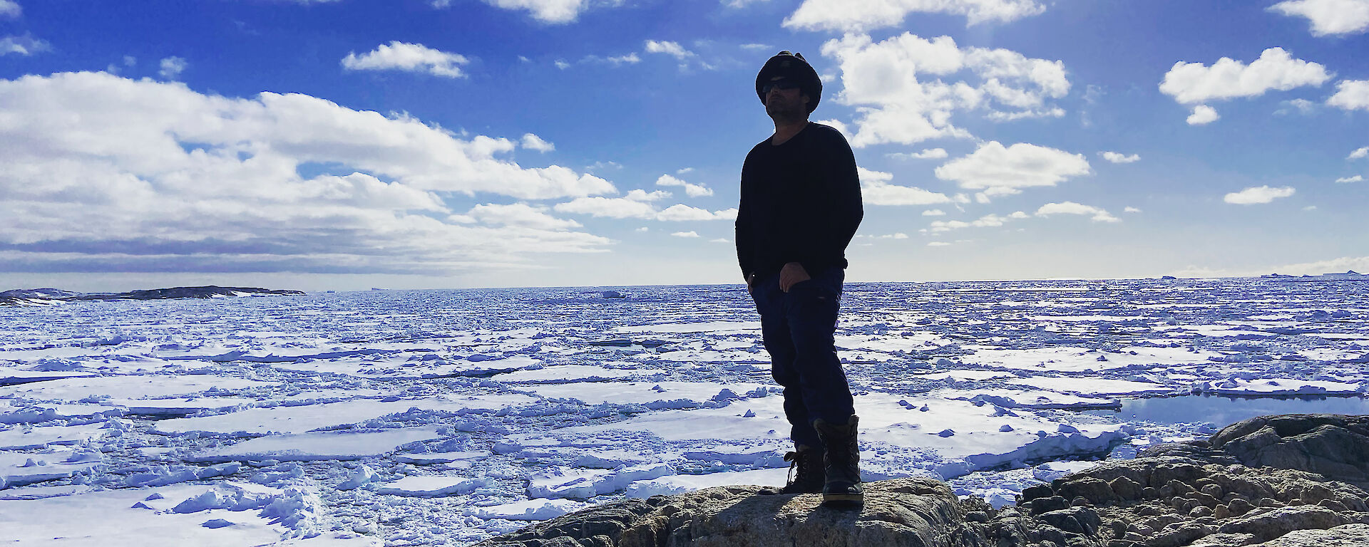 A person stands on a rock looking out of snow and water