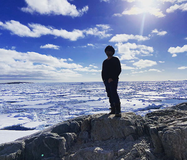 A person stands on a rock looking out of snow and water