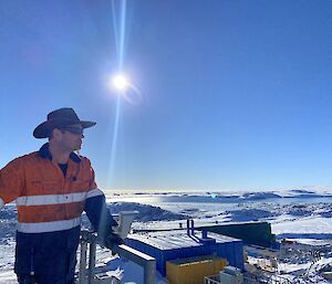 A man wearing high vis and a slouch hat under blue sky with snow around