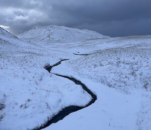 Snow covered valley with creek cutting it's way down the slope and through the snow