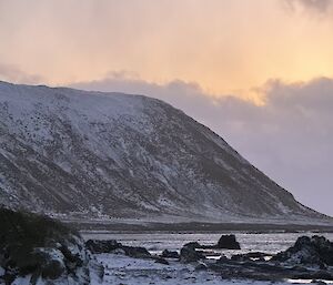 Looking across west beach to the bay and mountain in distance, everything has an orange/pink glow in the sunset's light