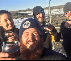 A group of four smiling people with the man in front holding a glass of red wine