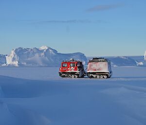 A red hagglund tractor stands on ice under blue sky with icebergs in the background