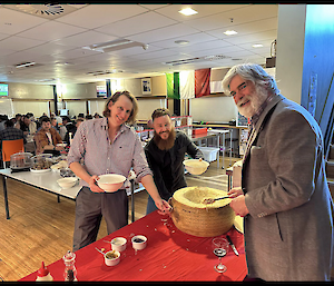 A man stands near a large cheese wheel on a table with a red tablecloth