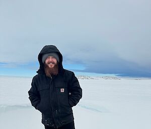A man in black hoody stands on an icy knoll