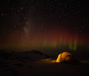 A tent lit up at night with an aurora in the background near Mawson station