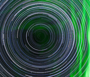 A full star trail looking down the south celestial pole with a vivid green aurora to one side