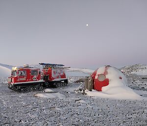 A red Hägglands tractor on the left of a red round fibreglass hut in the snow