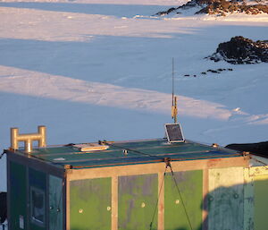 A green hut in the snow with an antennae and solar panel on the roof