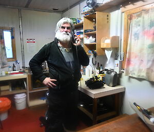 A man with a beard stands in a hut on the phone