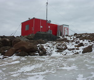 A red hut on a rocky hill with snow in the foreground