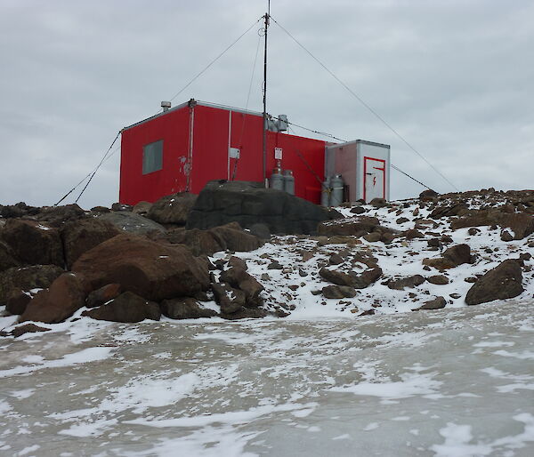 A red hut on a rocky hill with snow in the foreground