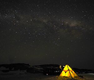 The Milky Way above a tent glowing from within near Macey hut