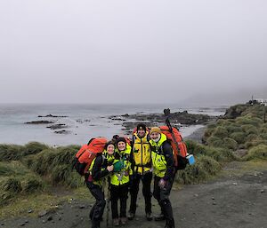 A group stand on a gravel road with sea and mist behind them