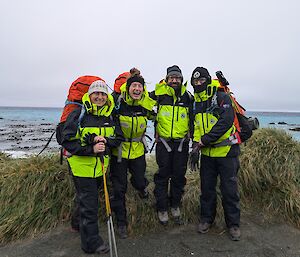 Four people in outdoor gear stand on a gravel road with the sea behind them