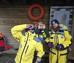 Three people in yellow outdoor gear stand on the verandah of a timber building