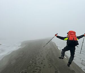 A person kicks their heels walking along a grey beach in the mist