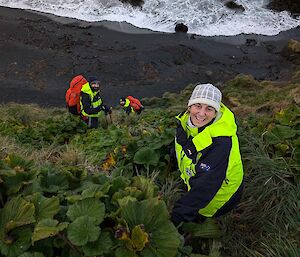 Two people smile at the camera while walking down a sleep slope with cabbage plants
