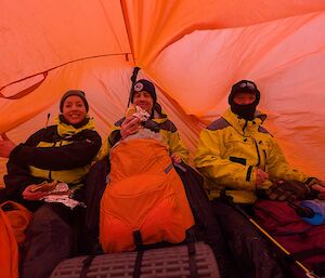 Three people inside a red tent
