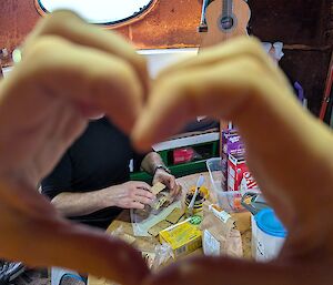 A person makes a heart shape with their hands inside a hut