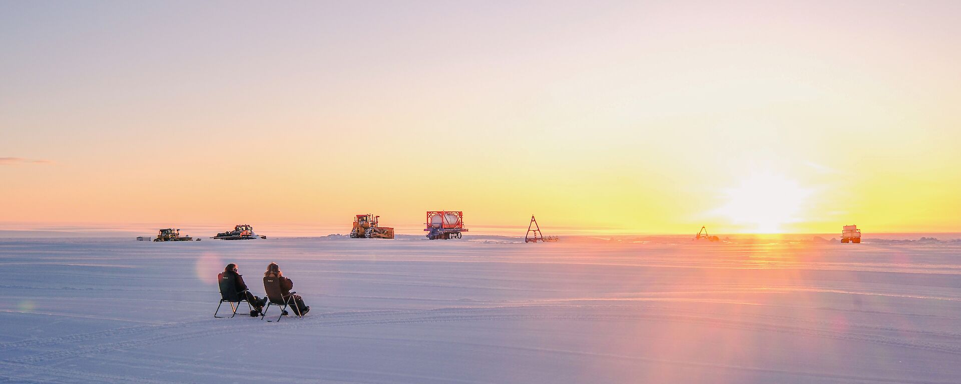 two expeditoner sit on fold out chair on the Wilkins runway on-looking the gorgeous sunset before the sun drops below the horizon
