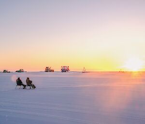 two expeditoner sit on fold out chair on the Wilkins runway on-looking the gorgeous sunset before the sun drops below the horizon