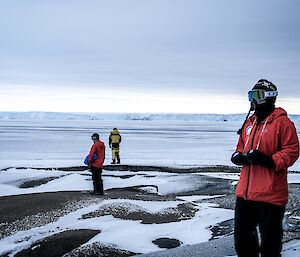 three expeditioners mindfully wandering the rocky outcrop down by a shore line close to station