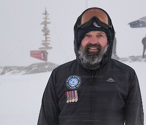 an expeditioner proudly sporting his grandfathers Anzac medals on Anzac outside with the Casey sign in the background and snow blowing through