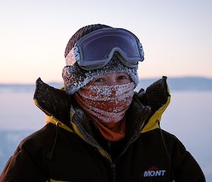 an expeditioner with an ice ridden face buff stops for a photo