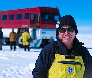 a expeditioner smiles for a photo taken on the journey down to station on a stunning clear skied day with the 'terra bus' transport in the backround
