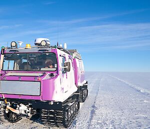 a Hagglund vehicle on a wide open 'snow road' with flat snow ground into the what seems never ending distance