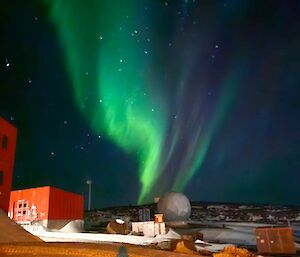 A green swirly aurora over a red shed and dome structure