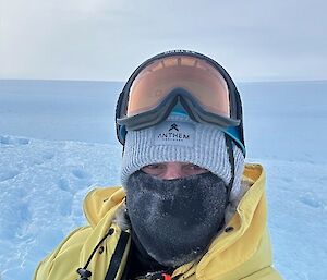 Andrew Brock in yellow outdoor gear and snow goggles on head, standing on a snowy slope