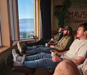 A row of dudes in chairs looking out the window on a sunny day