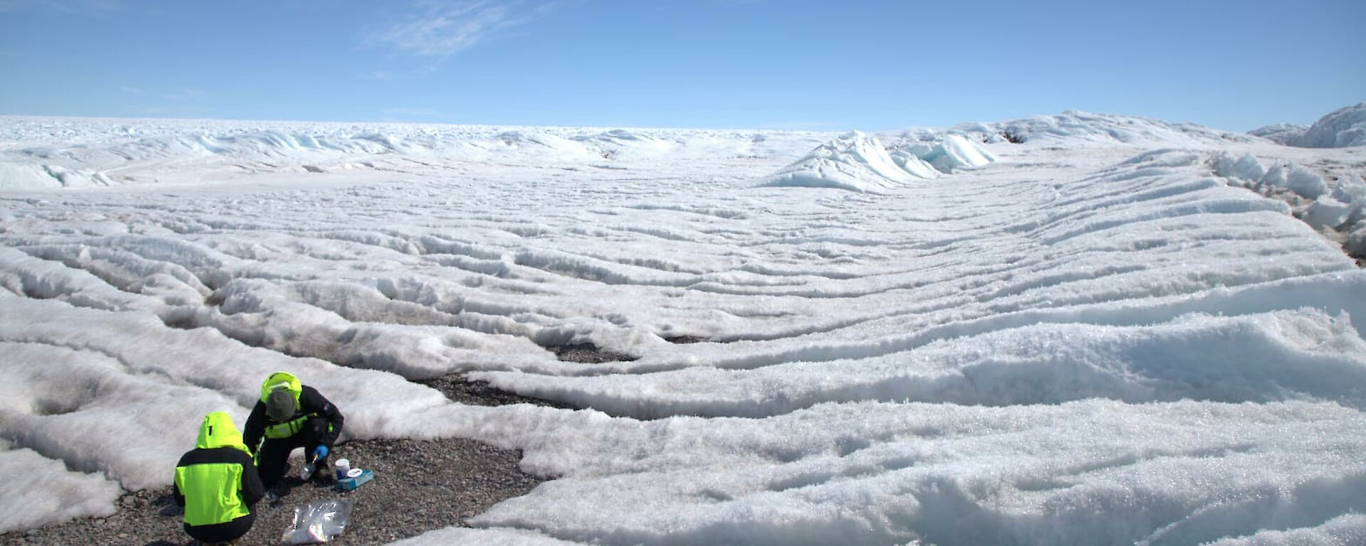 Two people on a ridged icy plain collecting samples
