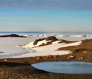 A group of red melon huts on a rocky hillside with snow and rocky outcrops in the background