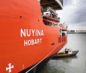 The rear of a large red and white ship with Nuyina Hobart.  A small dinghy is seen just in front.