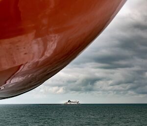 A large red ship bow covers the left of image and a small ferry on the horizon