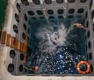Looking in to a deep pool with two people floating in it and one just entering the water with a splash