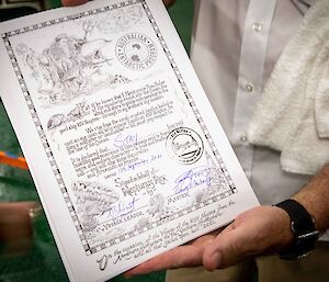 A close up of a person holding up a certificate from King Neptune congratulating them on crossing the equator