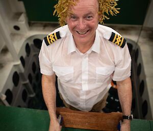 A man standing at the top of some ladders, exiting a pool of water with his captains uniform on and seaweed on his head