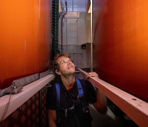 A man stands in a narrow passageway between two large orange keels