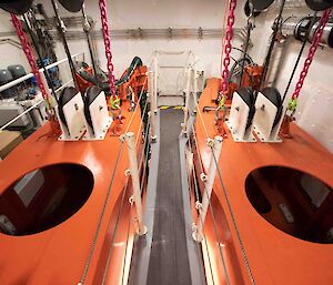 Looking down at the orange top side of two large keels hanging from chains in a housing room