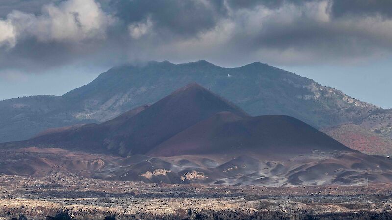 A view from the ship of a mountainous island coloured red from the volcanic soil