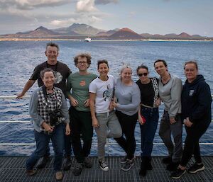 A group shot standing by the ship handrail with Ascension Island in the background