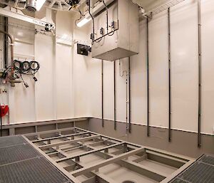 A room inside a ship with metal grids on the floor and a sunken area with a hole in it